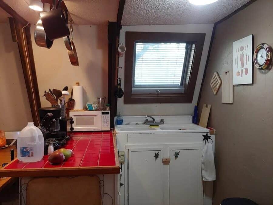 Compact kitchen in a tiny house with white cabinets, a small window, and essential appliances.