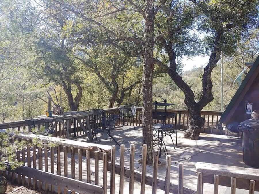 A-frame cabin surrounded by trees in Fort Davis, Texas, with a spacious outdoor deck and seating are.