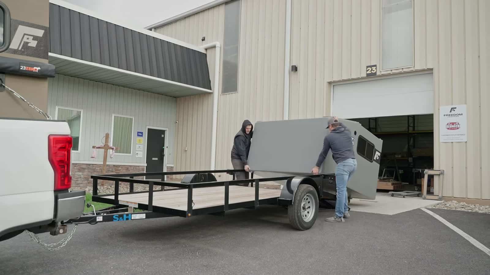 Two people loading a Freedom Camper onto a utility trailer