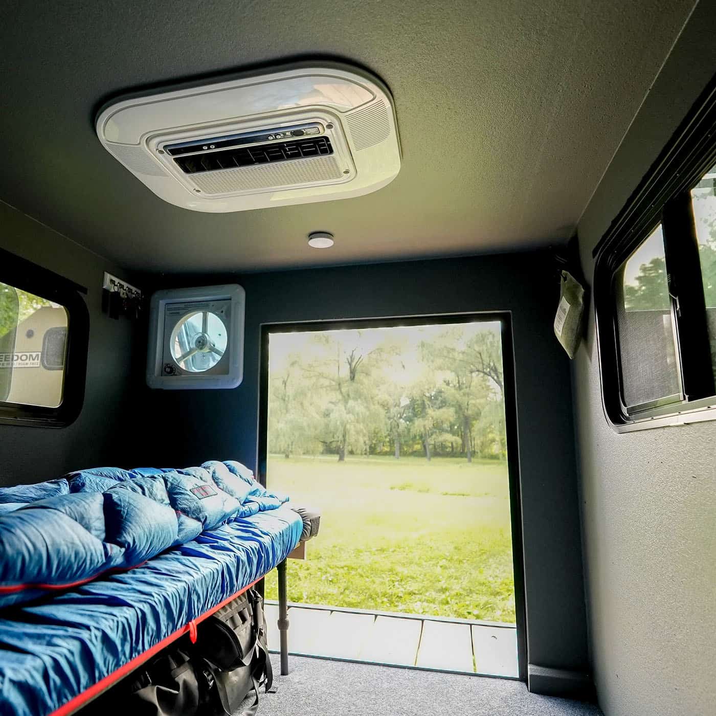 Inside a Freedom Camper with a mattress, 12V fan, and rooftop air conditioner