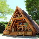 A-frame tiny house with a netted balcony and wooden exterior, nestled among lush green trees.