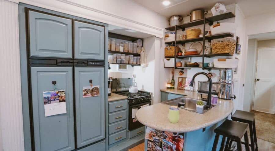 Compact tiny house kitchen with blue cabinets and open shelving.