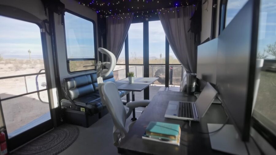 Interior of a toy hauler converted into a cozy workspace with large windows and scenic views.