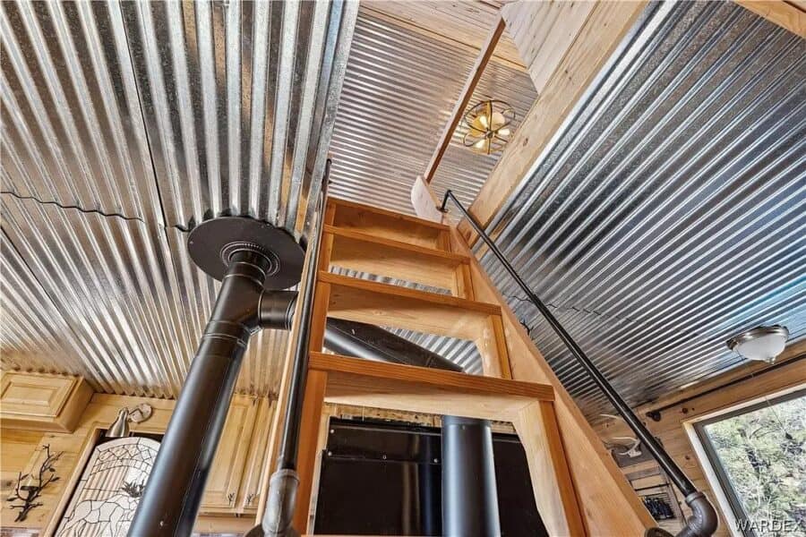 Interior view of a tiny house loft with metal ceiling, wooden stairs, and cozy rustic decor.