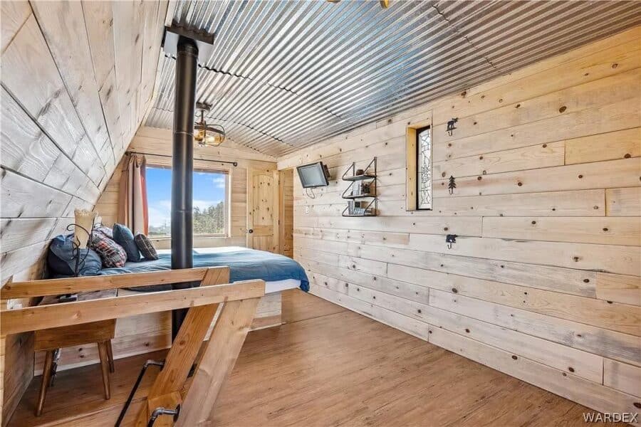 Charming tiny cabin interior featuring wooden walls, a cozy bed, and mountain scenery visible throug.