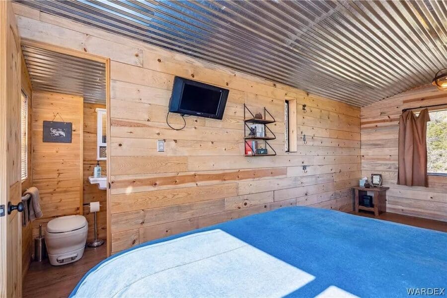 Cozy tiny house bedroom with wood-paneled walls and mountain scenery visible through the window.