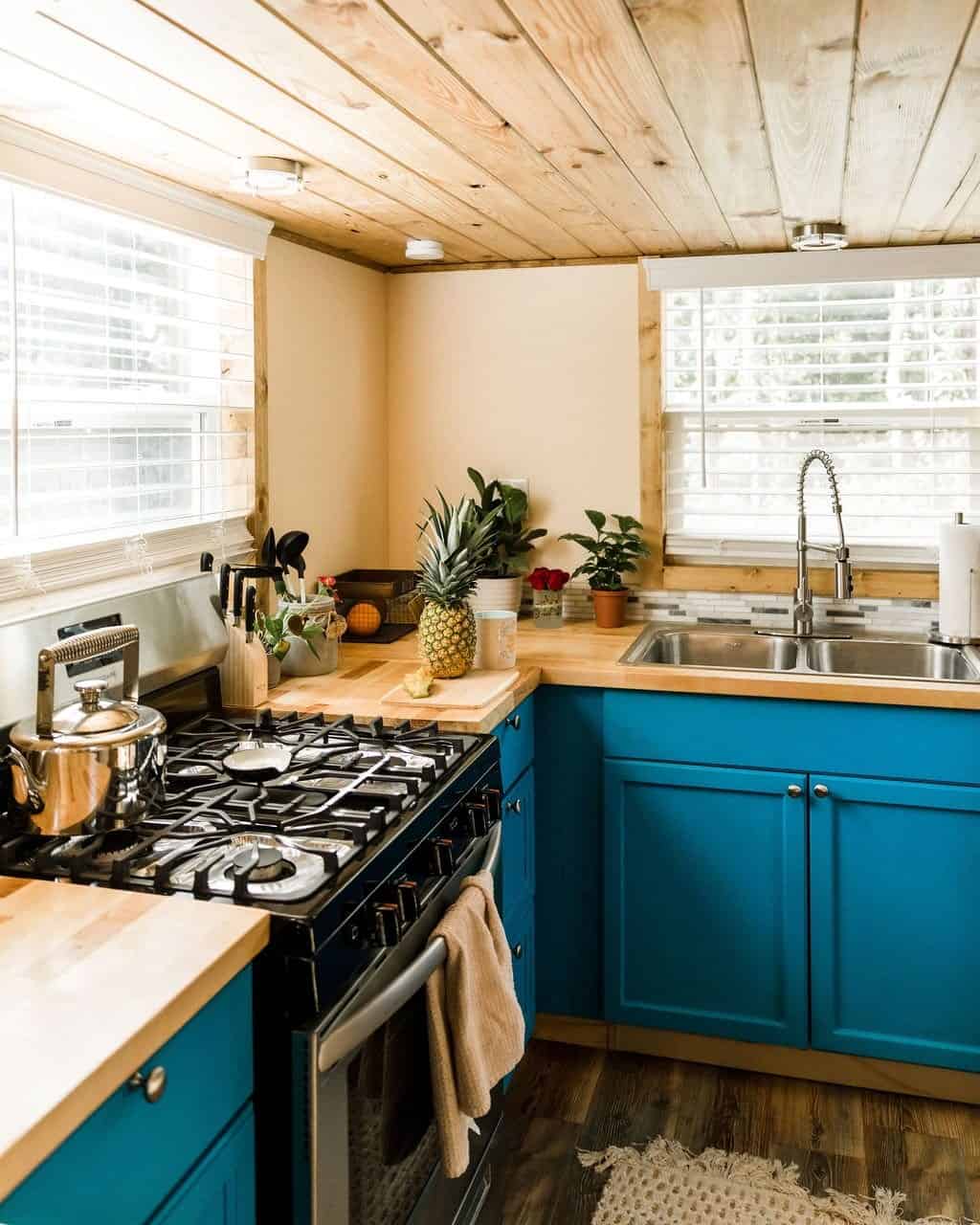 Goa tiny house kitchen with a full-size range and oven, butcher-block counters, a double stainless sink, and blue cabinets under a pine ceiling