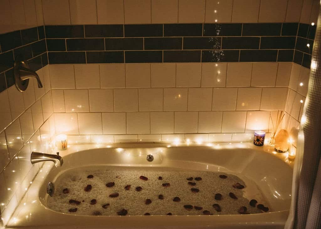 Full-size soaking tub in the Goa tiny house bathroom with subway tile, candles, and string lights