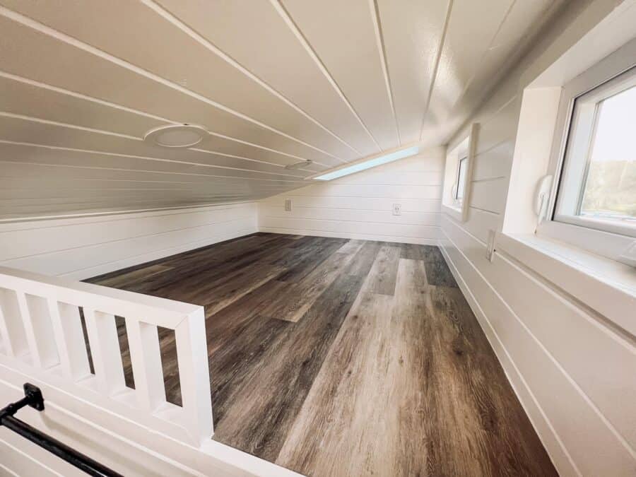 Interior view of a tiny house bedroom with sloped ceiling and wood flooring.
