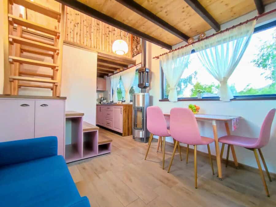 Cozy tiny house interior with pink chairs and mountain view through large windows.