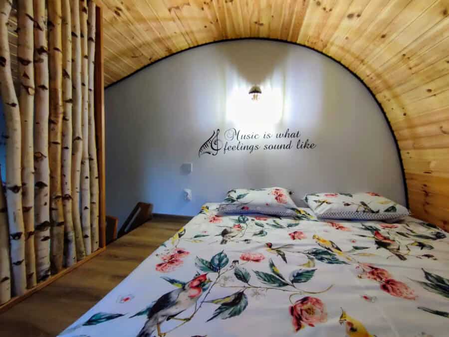 Cozy tiny house bedroom with wooden ceiling, floral bedding, and wall quote about music.