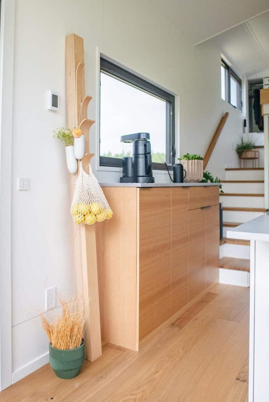 Modern tiny house kitchen with wooden cabinets, large window, and minimalist decor.