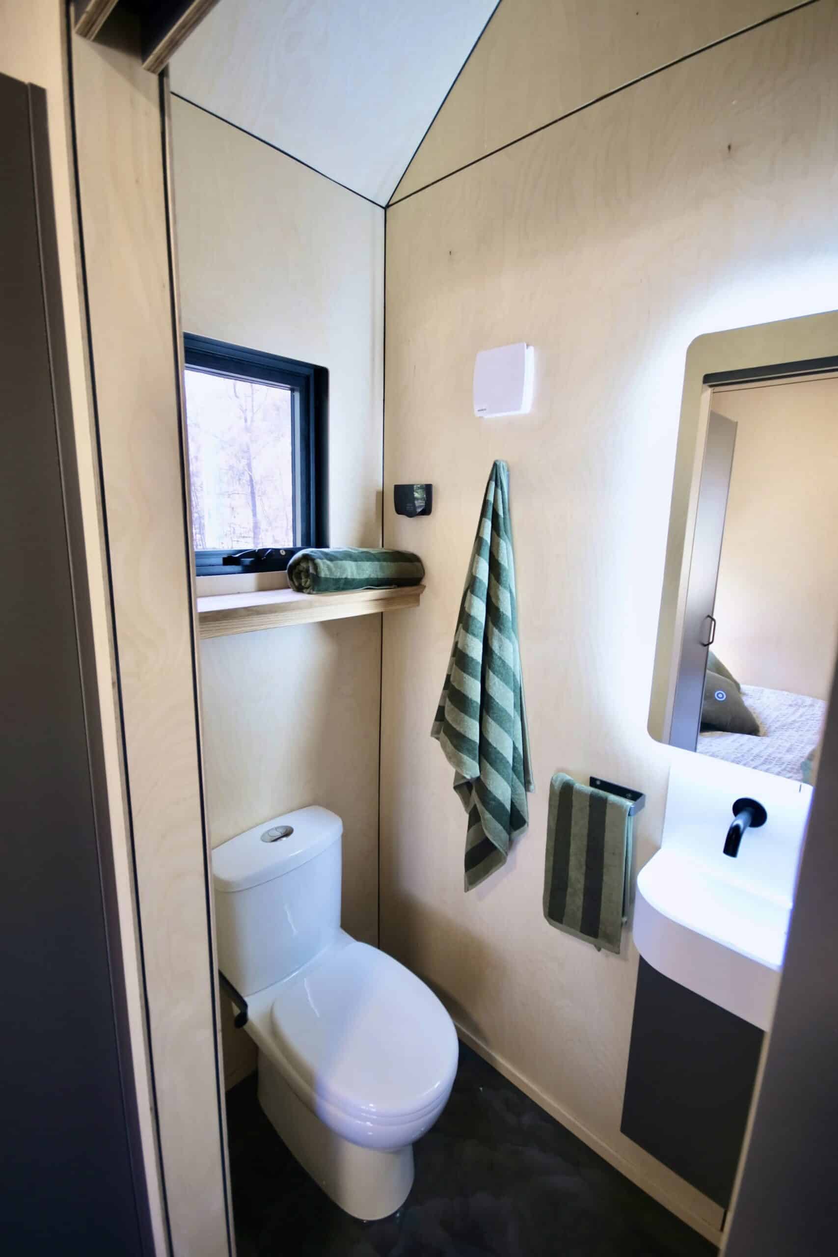 Bathroom in the Eire tiny house with glass shower, stone vanity and backlit mirror