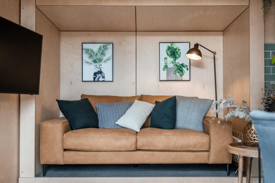 Cozy living room inside the Luna tiny house with a tan sofa, pillows, and botanical wall art.