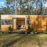 Tiny house on wheels with wooden exterior in a forest setting.