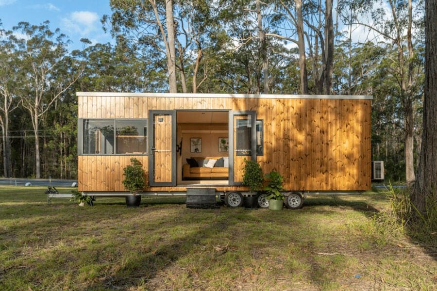 Tiny house on wheels with wooden exterior in a forest setting.