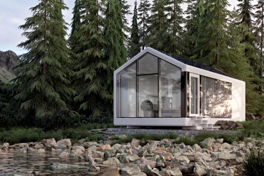 Modern tiny house with large glass windows surrounded by trees and rocky landscape.