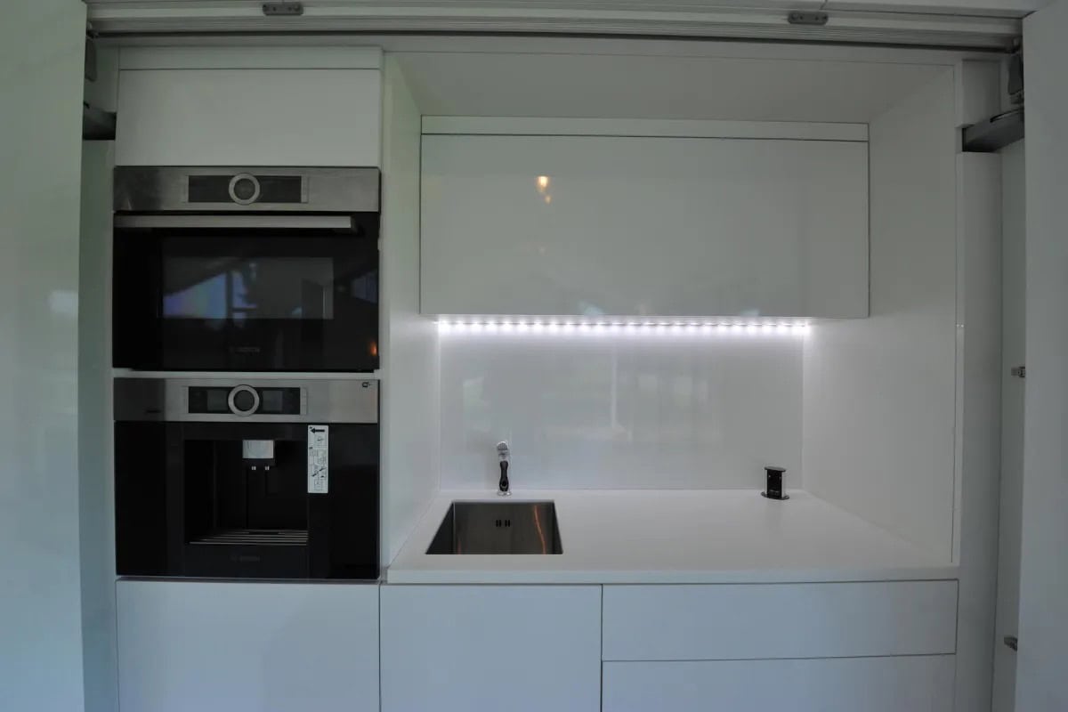 Modern tiny house kitchen with sleek white cabinetry and integrated appliances.