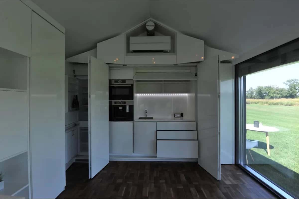 Modern tiny house kitchen with compact appliances and large glass door.