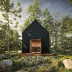 Small black Scandinavian-style cabin with wooden porch in lush forest setting.