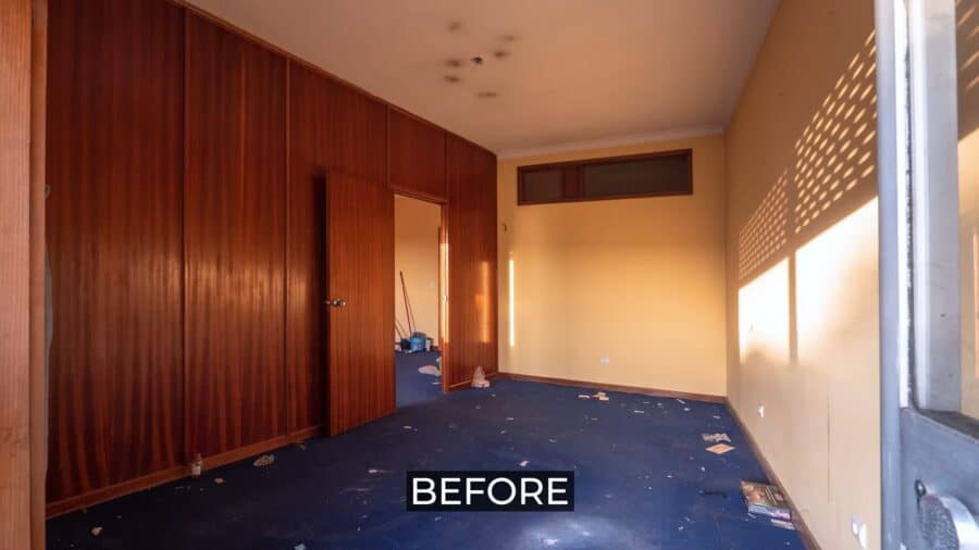 Interior of a small apartment before renovation, showing worn carpet and outdated wood paneling.