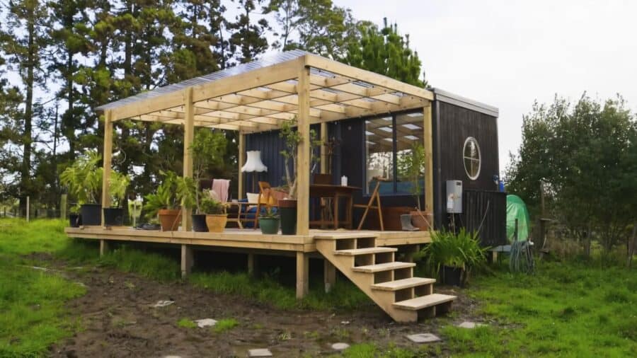 Small modern tiny house with a porch, surrounded by greenery, ideal for minimalist living.