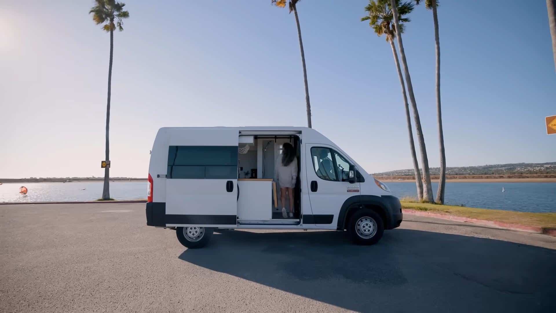 Compact van converted into tiny home with shower and convertible bed by the water.