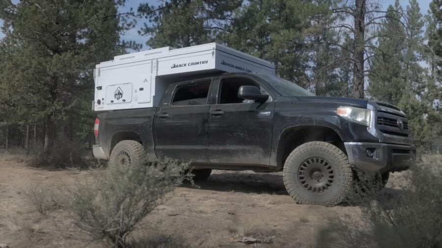Black truck camper on a rugged off-road vehicle in a forest setting.