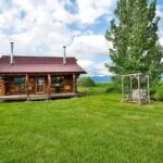 Rustic log cabin in Montana with lush green lawn and scenic landscape.