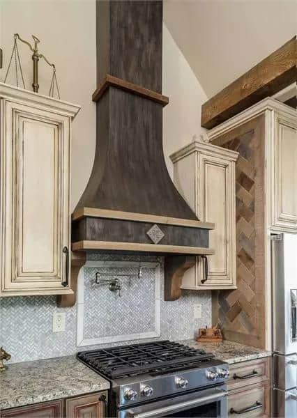 Charming tiny house kitchen featuring a rustic wooden range hood and vintage cabinetry.