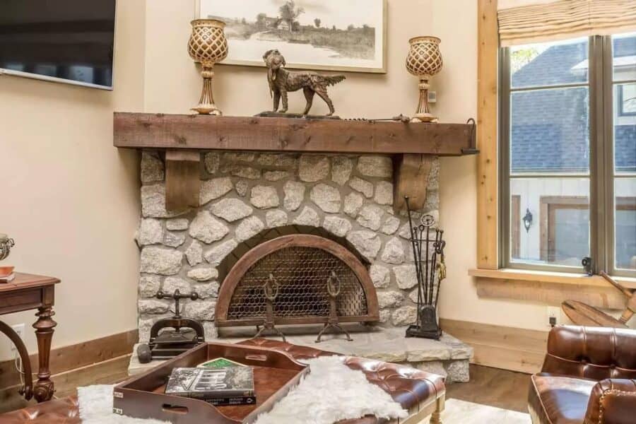 Fireplace with stone surround and wooden mantel in a cozy, rustic living room setting.
