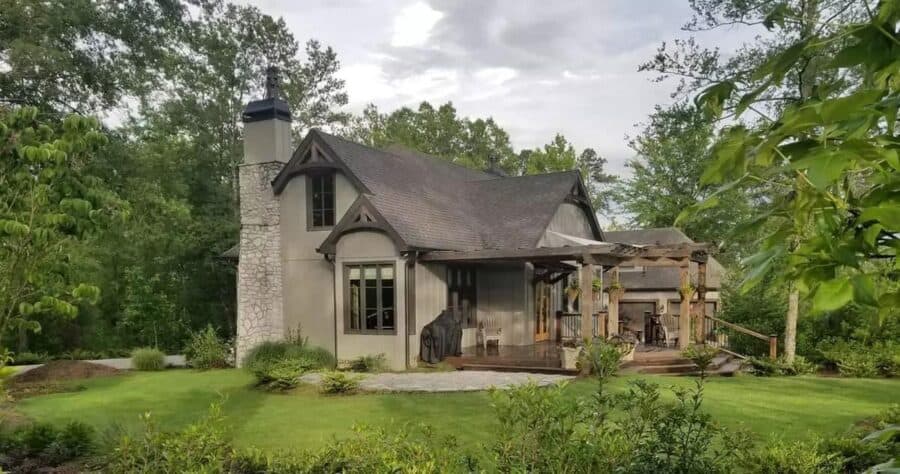 Charming tiny house with stone chimney and lush garden setting, perfect for small space living.