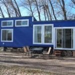 Compact blue tiny house with large windows and outdoor seating, perfect for a mobile lifestyle and e.