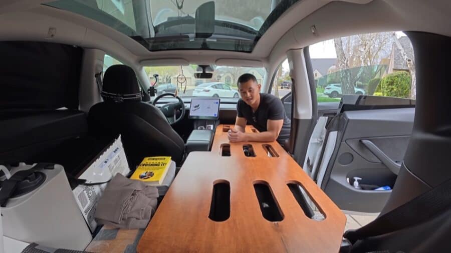 Interior view of a converted Tesla camper van with custom wood table and modern amenities.