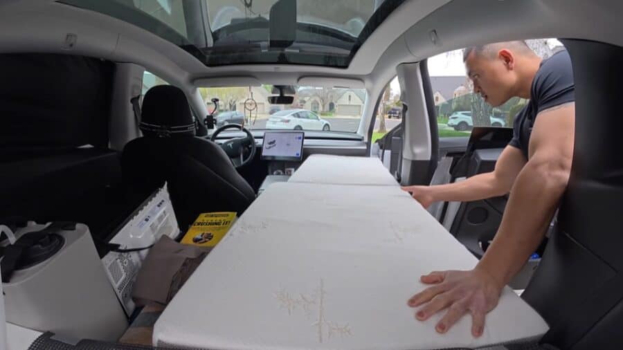 Man adjusting mattress inside a converted Tesla camper van.
