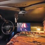 Cozy Tesla camper interior with a bed, monitor, and ambient lighting for nomadic living.