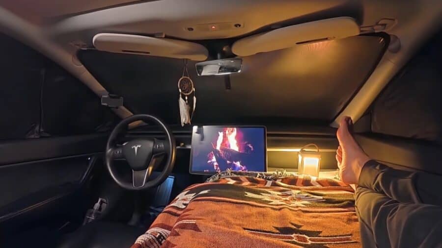 Cozy Tesla camper interior with a bed, monitor, and ambient lighting for nomadic living.