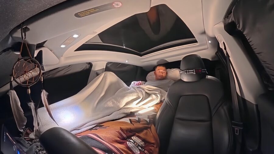 Interior view of a cozy Tesla turned into a stealth camper with a sleeping area.