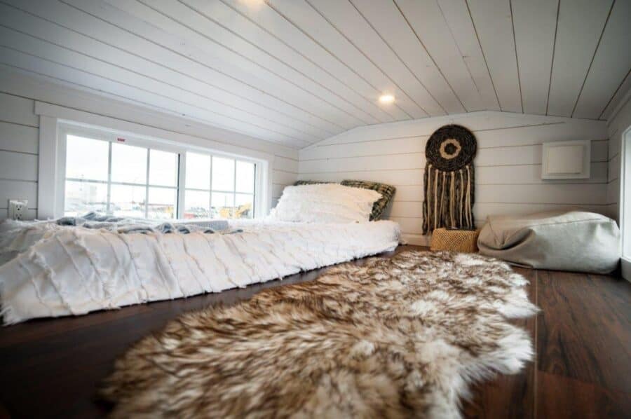 Compact tiny house bedroom with white shiplap walls and natural light.
