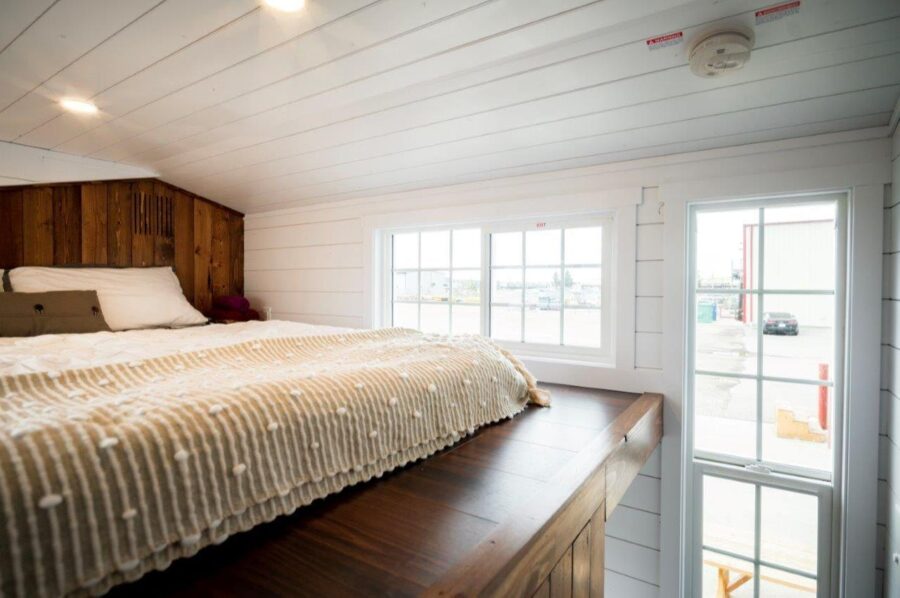 Compact tiny house bedroom with large windows and cozy interior design.