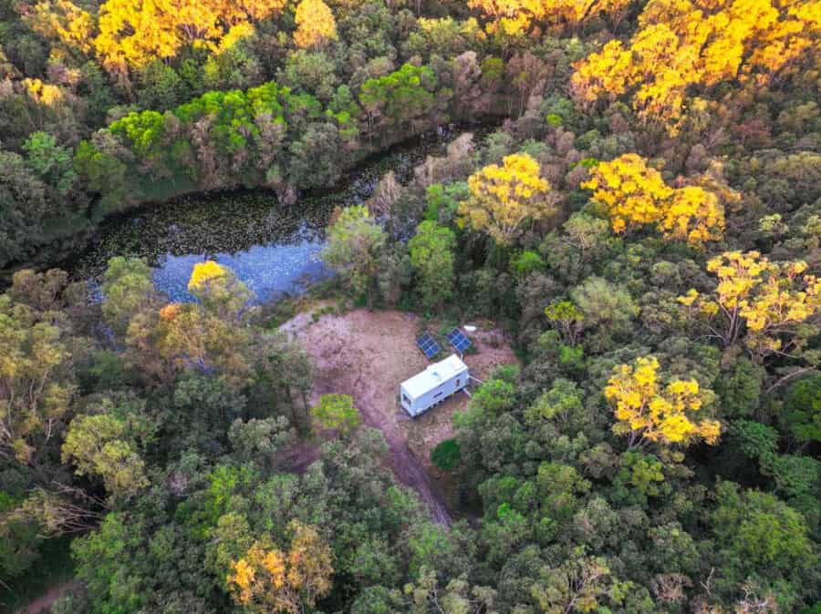 Tiny house surrounded by lush forest and a small pond in rural Queensland.