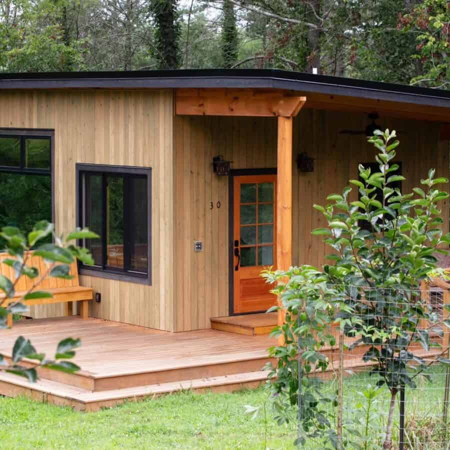 Charming tiny house with wooden exterior and front porch in a lush green setting.