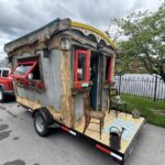 Colorful tiny house with red window frames and rustic wood accents on a trailer.
