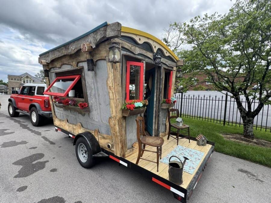 Colorful tiny house with red window frames and rustic wood accents on a trailer.