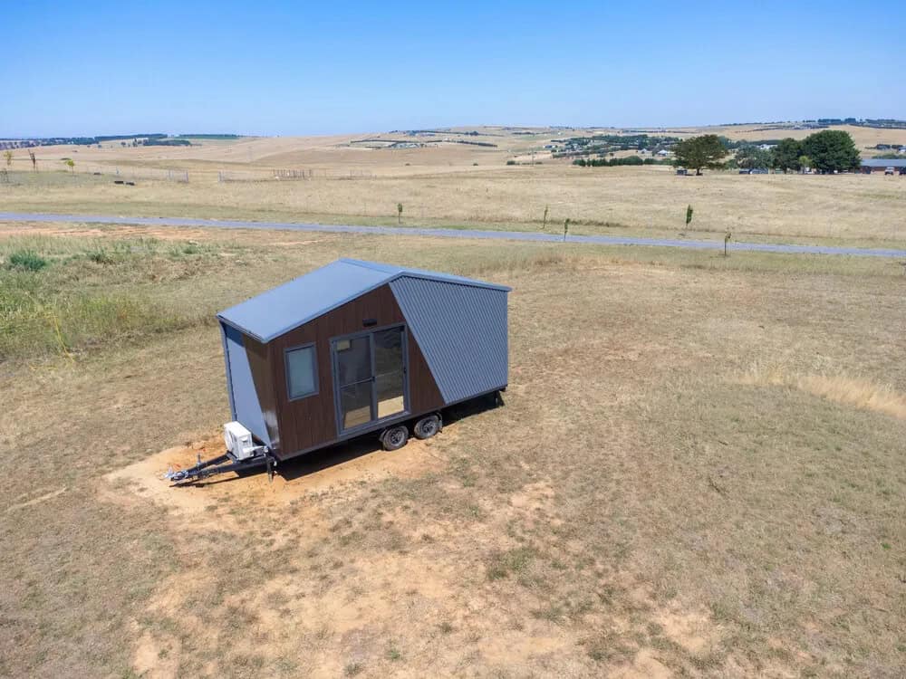 Aerial view of the Joey tiny house showing its compact 6-meter footprint, dual-axle trailer, drawbar, and the corrugated Colorbond roof sweeping over the gable end