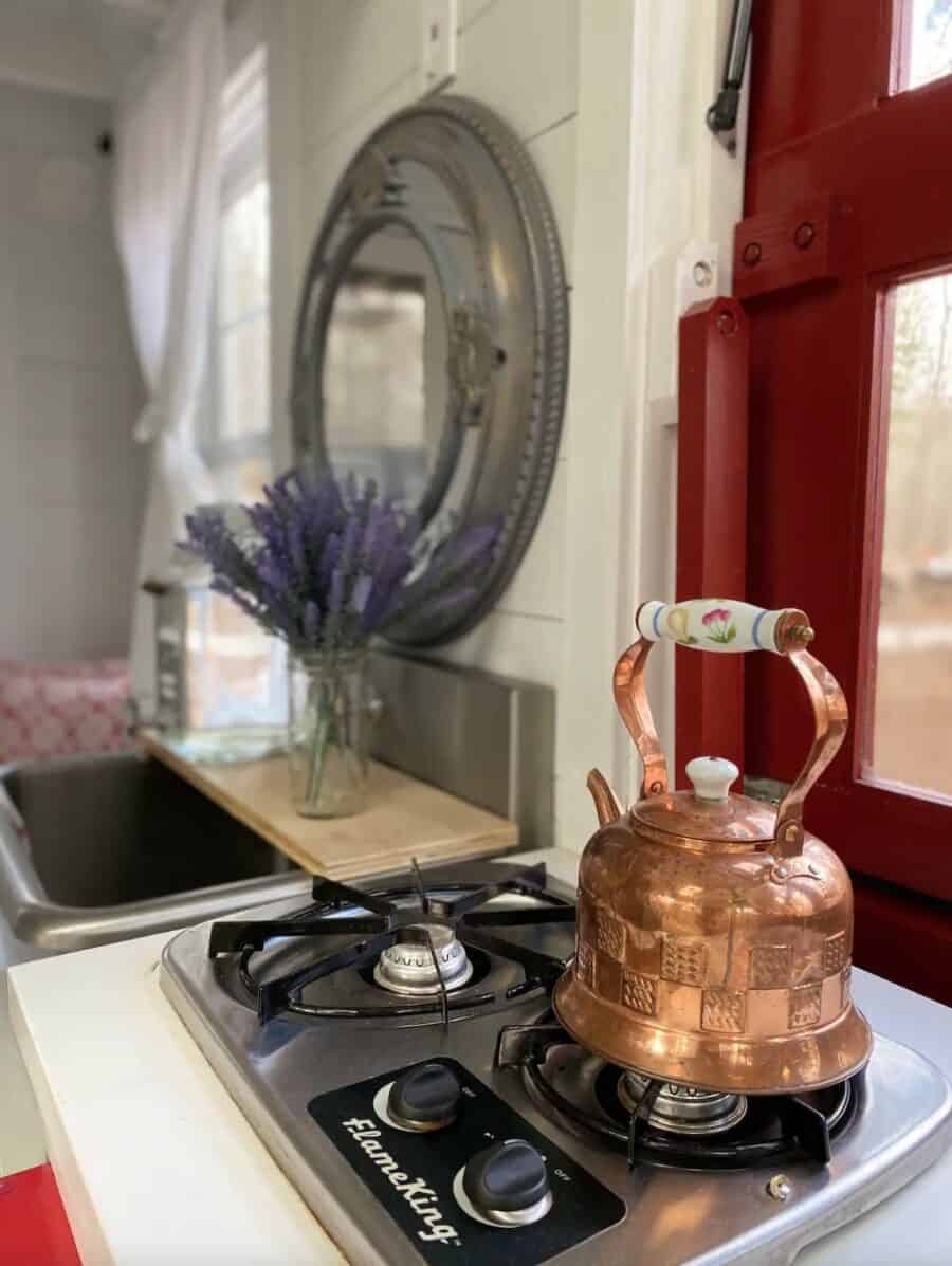 Tiny house kitchen with copper kettle on stove, lake view, and rustic decor.
