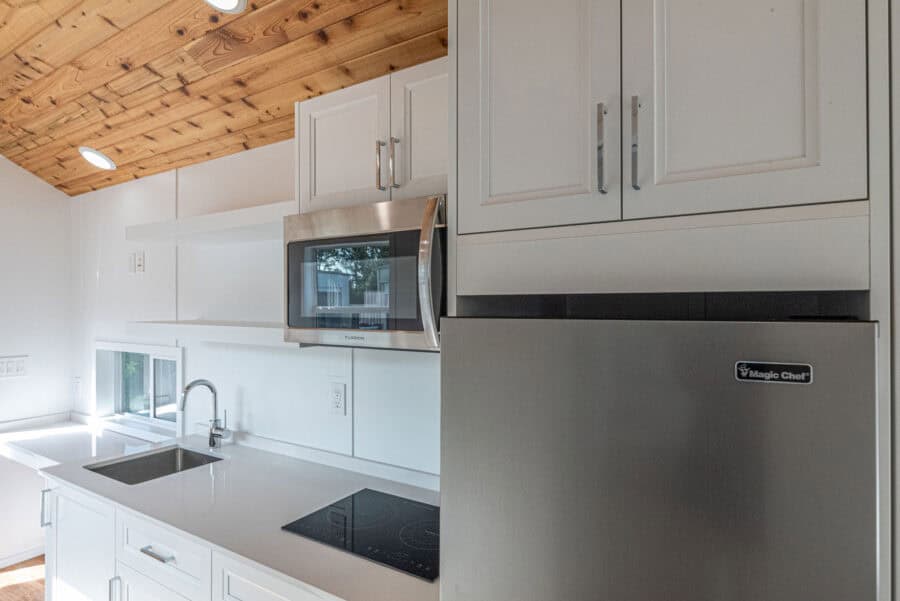 Bright tiny house kitchen with white cabinets and modern appliances.