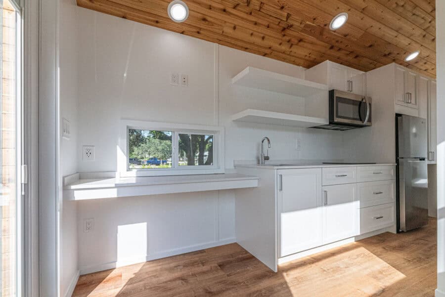 Modern tiny house kitchen with white cabinetry and natural wood ceiling.