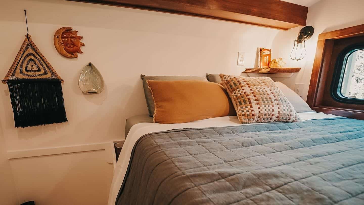 Lofted queen bedroom with a porthole-style window, wall sconce, and earthy bedding