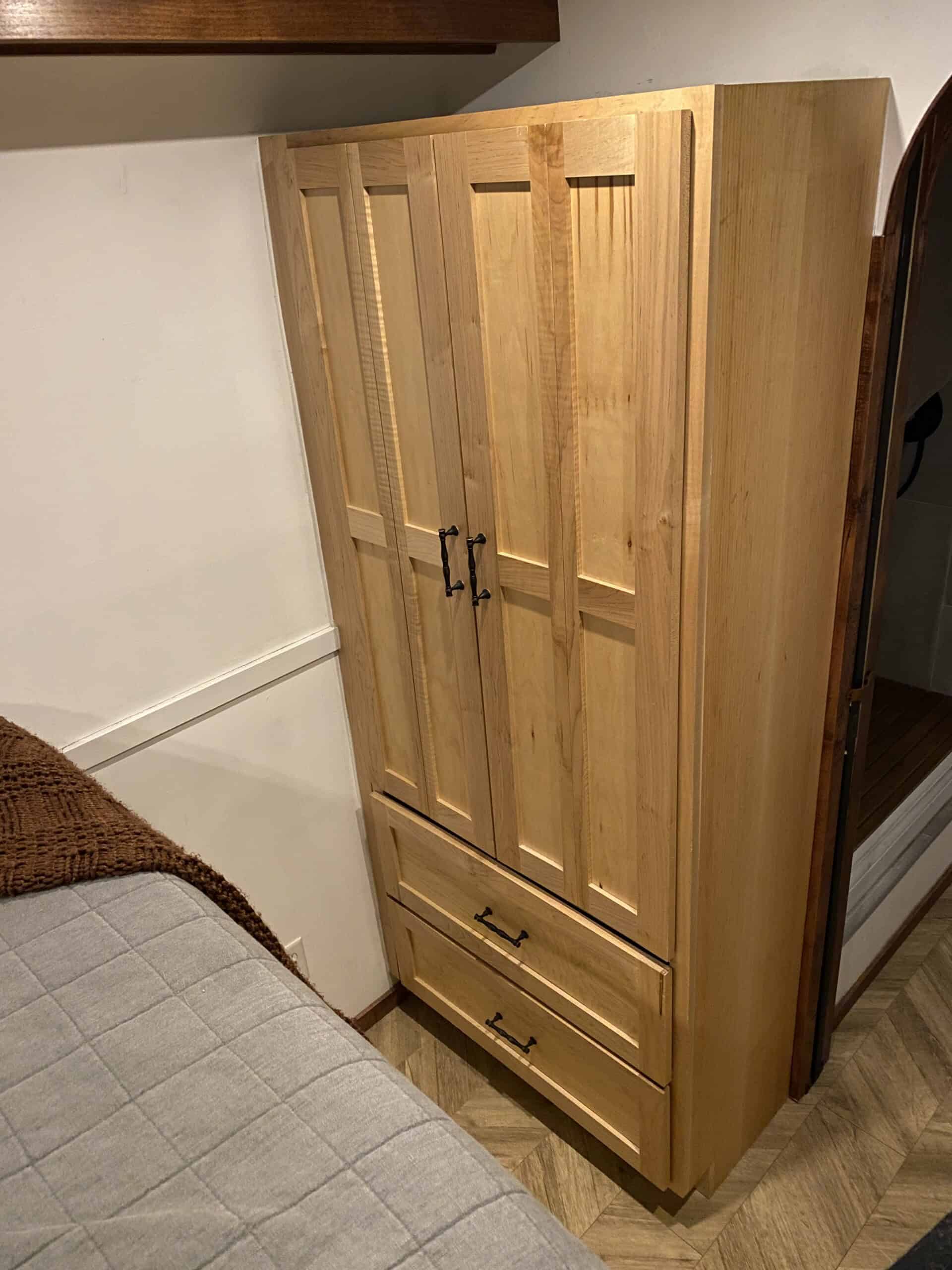 Closed ambrosia-maple wardrobe with two doors and lower drawers beside the bed